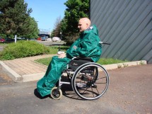 Photo représentant une personne en fauteuil roulant manuel et portant une cape verte de pluie